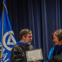 Provost Mili shakes hands with man as he holds his certificate